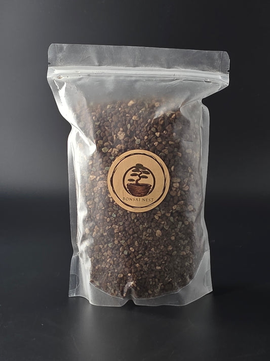 Sealed clear pouch of dark brown granular soil mix lying flat on a dark surface, wooden Bonsai Nest label on the front.