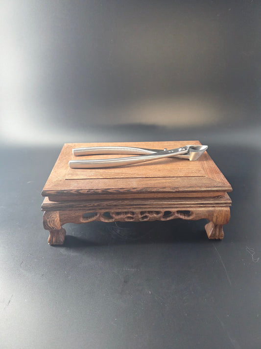 Silver bonsai concave cutter standing upright against a wooden block, showing its curved head