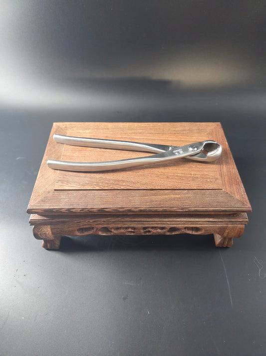 Silver bonsai knob cutter standing upright against a wooden block, showing its round head