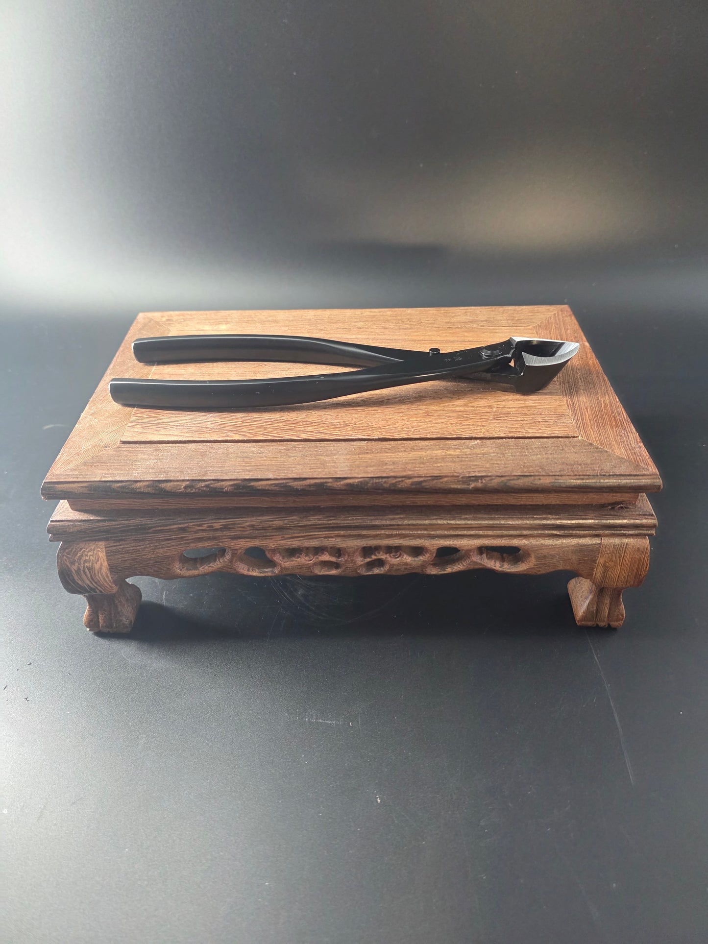 Black bonsai concave cutter standing upright against a wooden block, showing its curved head