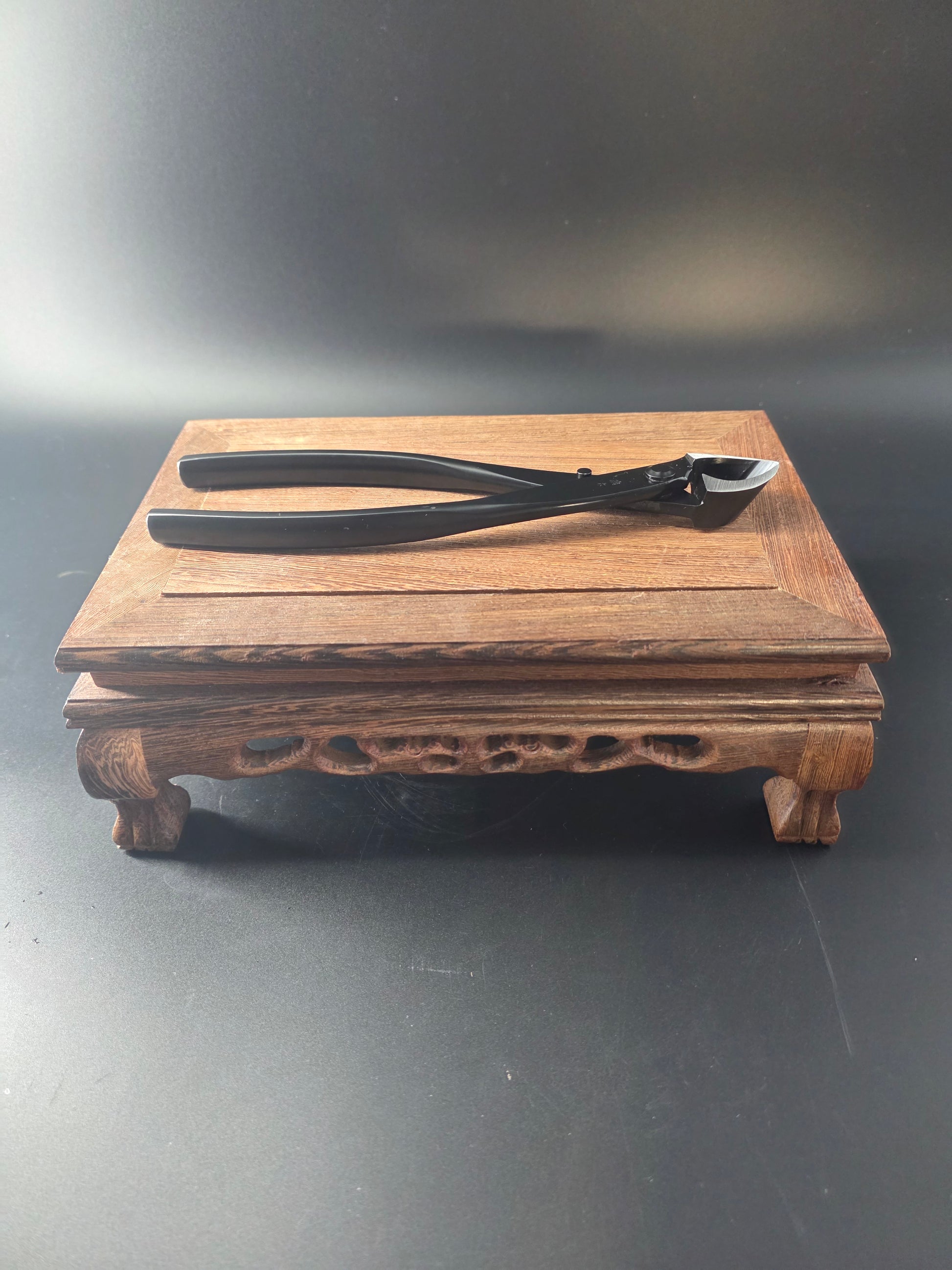 Black bonsai concave cutter standing upright against a wooden block, showing its curved head