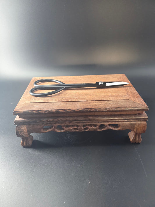 Black bonsai pruning scissors standing upright against a wooden block
