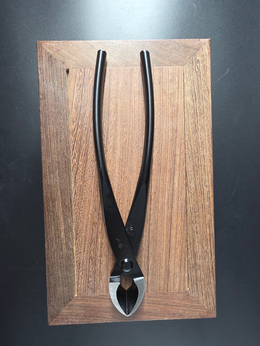 Black bonsai concave cutter with a curved cutting head and long handles, laid flat on a wooden board