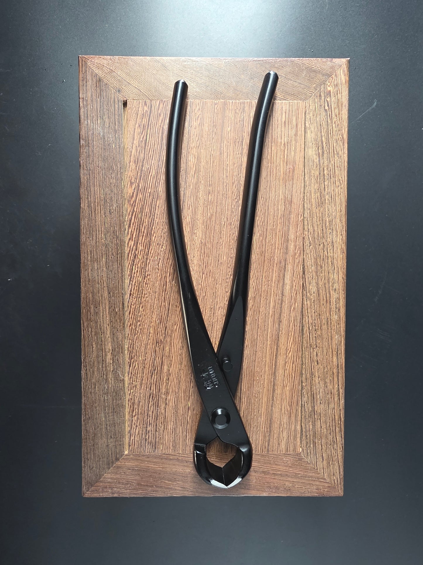 Black bonsai knob cutter with a round head and long handles, laid flat on a wooden board