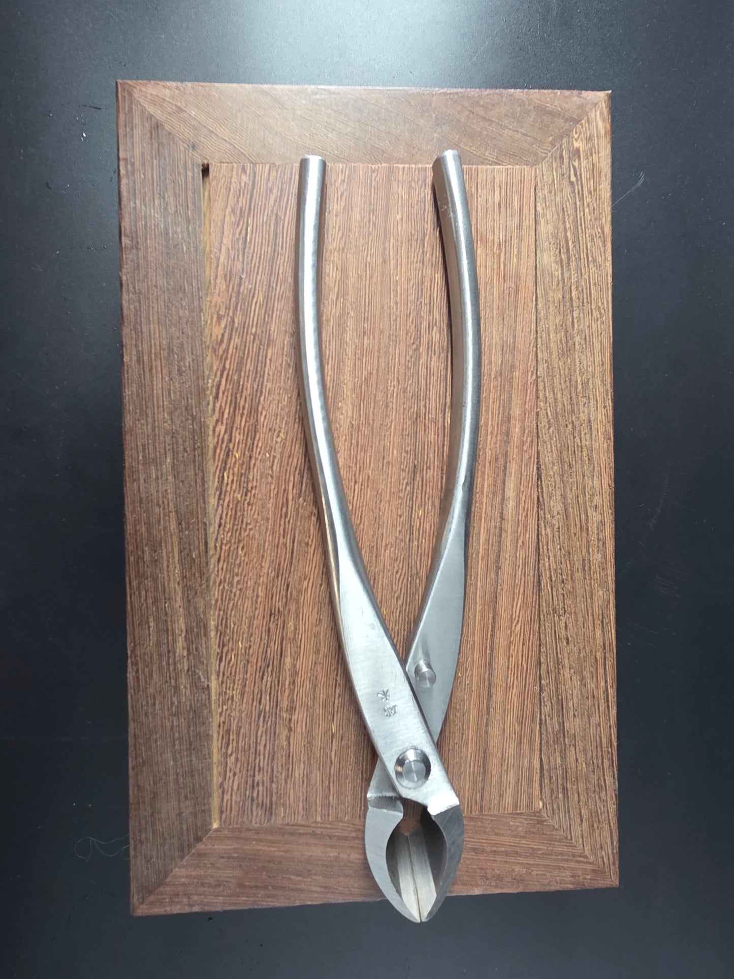 Silver bonsai concave cutter with a curved cutting head and long handles, laid flat on a wooden board