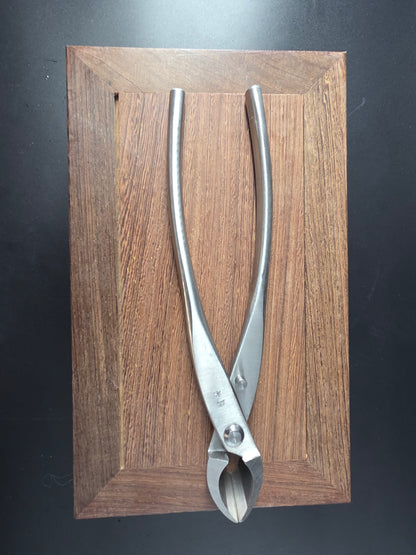 Silver bonsai concave cutter with a curved cutting head and long handles, laid flat on a wooden board