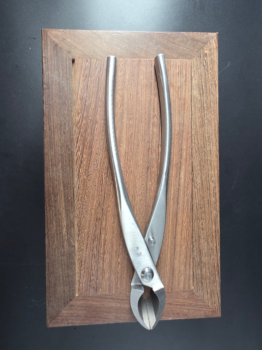 Silver bonsai concave cutter with a curved cutting head and long handles, laid flat on a wooden board