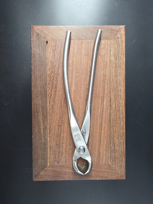Silver bonsai knob cutter with a round head and long handles, laid flat on a wooden board
