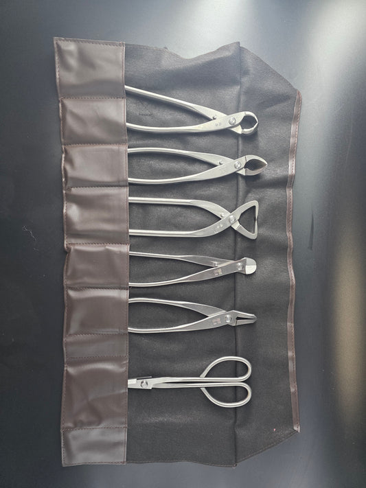 Six silver bonsai tools in an open roll: pruning scissors, concave cutter, knob cutter, wire cutter, jin pliers, root cutter